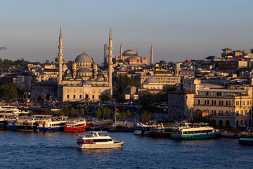 Obraz premium A serene Istanbul cityscape at sunset from the Halic Bridge, featuring the silhouettes of Hagia Sophia and the New Mosque with ferries on the calm Golden Horn waters. Istanbul, Turkey.