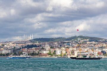 Obraz premium A dramatic view of Istanbul's Asian shore from the Bosphorus, with ferries, Camlica Hill, the Turkish flag and mosque under stormy skies. Istanbul, Turkey.