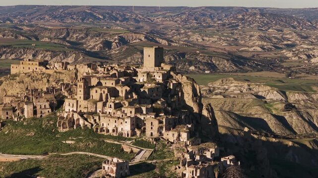 Aerial view of the ancient, crumbling architecture of Craco, a ghost town perched atop a hill surrounded by a barren, undulating landscape, Craco, Basilicata, Italy.
