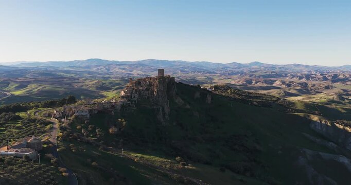 Aerial view of the old town of Craco, a ghost town perched high on a steep, rugged hillside, its stone buildings bathed in the soft glow, Craco, Basilicata, Italy.
