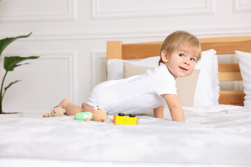 Cute little boy playing with toys on bed at home