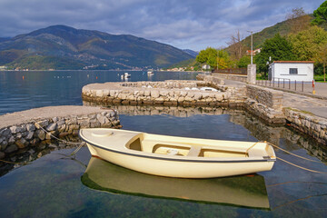 Beautiful autumn Mediterranean landscape. Montenegro, Adriatic Sea. View of Bay of Kotor near Tivat city on cloudy day. Fishing boat in small harbour.  Donja Lastva village