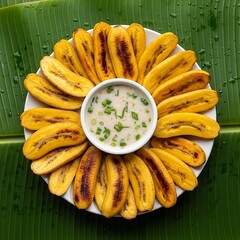 A plate of fried plantains with a white dipping sauce on a banana leaf surface