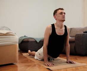 A man performs a cobra yoga pose on a mat in his bedroom. The scene highlights morning stretching concept.