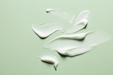 Aesthetic flat lay of creamy white textures on a soft green background, showcasing smooth and glossy skincare products.