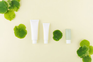 A minimalist flat-lay featuring skincare products in white tubes and a small bottle, surrounded by vibrant green leaves against a soft yellow background.