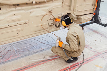 Specialist spraying anti rust sealant into the hidden chassis cavities. Protection against corrosion and internal body element sealing in a professional auto service shop