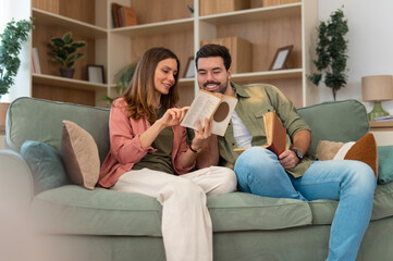 Obraz premium Couple relaxing on sofa reading book together at home