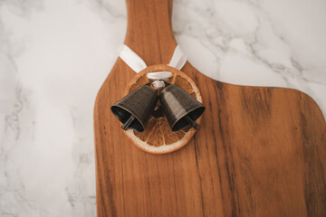 A rustic wooden cutting board sits elegantly on a marble surface. It features decorative bells and a slice of dried orange tied with a ribbon, adding charm to the kitchen