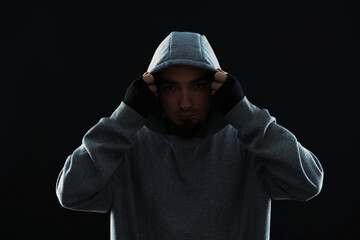 Criminal man in hood on black background