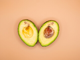 Two avocado halves arranged symmetrically side by side on a beige background, top view.