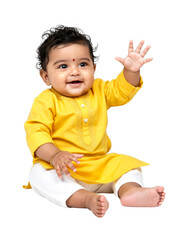 Cute Indian baby boy smiling happily and waving his hand while sitting comfortably wearing traditional yellow kurta and white pants.