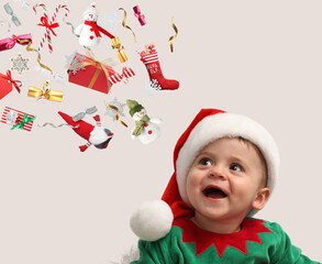 Cute little baby in elf costume looking at flying festive stuff on light grey background. Christmas...