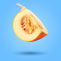 Piece of pumpkin in air on pale blue background. Gourd vegetable