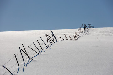 Landscape with snow-covered hills and windbreak fence