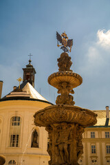 Fototapeta premium Ornate baroque fountain with eagle sculpture in Prague Castle courtyard featuring yellow palace buildings and chapel