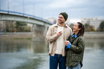Happy diverse couple drinking coffee by river