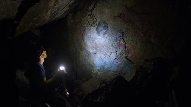 Explorer Illuminating Ancient Cave Paintings Inside Dark Cave