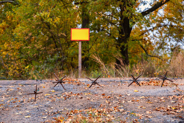 Barbed wire stands against a backdrop of vibrant autumn foliage near a warning sign in a remote area