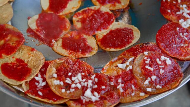 Mexican chalupas with red salsa cooking on a comal