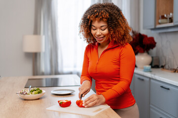 Happy young woman preparing fresh healthy salad, cutting vegetables in modern kitchen