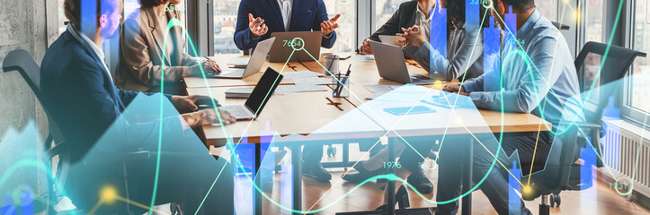 Five business professionals meet in a spacious office with large windows. They actively discuss ideas, using laptops, while sharing insights on strategies and goals in a collaborative setting.