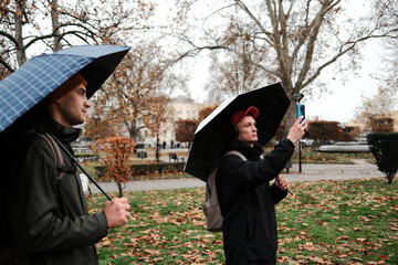 A man under an umbrella takes a photo with his smartphone in a rainy autumn park. The scene represents the concept of creativity and personal expression.