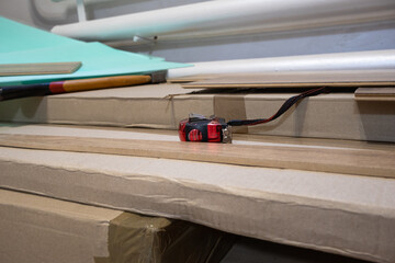 A measuring tool rests on top of stacked cardboard boxes, indicating preparation for a woodworking task in a workshop environment