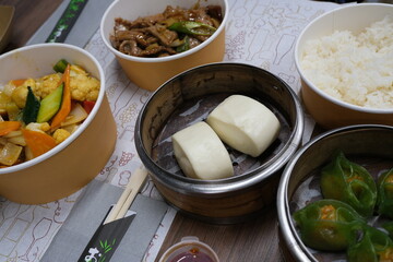 Assorted Asian dishes with steamed buns, vegetables, rice, and green dim sum.