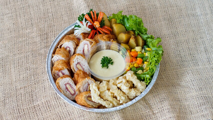 Top view of chicken cordon bleu platter with mixed vegetables, potatoes, crispy sides, and creamy sauce in a rustic setting. Perfect for catering, menus, food delivery, and promotional use.