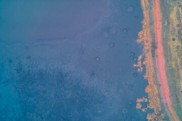 Aerial top down view of blue cracked sludge crust near red road. Industrial waste pollution texture and environmental danger background.