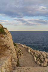 Vertical view of a winding stone coastal path on the cliffs of Saint-Jean-Cap-Ferrat, overlooking the deep blue Mediterranean Sea.
