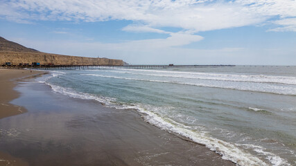Aerial view of Puerto Eten in Chiclayo, Lambayeque, showing the fishing pier, sandy beach, and calm Pacific coastline under clear skies