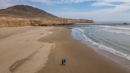 Aerial view of Puerto Eten in Chiclayo, Lambayeque, showing the fishing pier, sandy beach, and calm Pacific coastline under clear skies