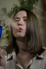 Young adult uses vape indoors, surrounded by indoor plants during the afternoon