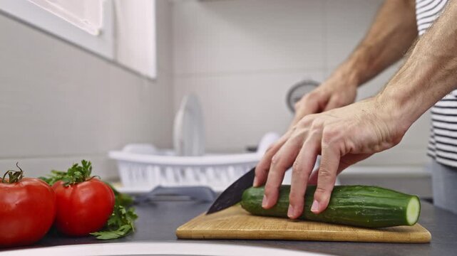 A person meticulously peels a fresh green cucumber using a vegetable peeler in a clean, modern kitchen.