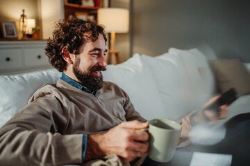 Man relaxing at home, smiling, watching tv, drinking coffee