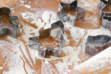 Baking gingerbread cookie cutters, wooden rolling pin, and flour are messily spread on rustic kitchen table. Process of cooking festive traditional Christmas sweets, bakery