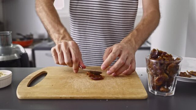 Close-up of hands carefully pitting fresh, sweet dates on a wooden cutting board in a kitchen setting, preparing them as a healthy snack or ingredient.