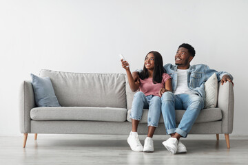 Split System. Satisfied African American woman holding remote control relaxing under the air...
