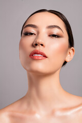 Glamorous portrait of a brunette woman showcasing flawless skin and elegant makeup against a grey...