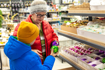 Boy and Elderly Woman Choosing Christmas Tree Ornament.  During Holiday Shopping – Intergenerational Bonding and Family Holiday Traditions.  preparation process for Christmas and New Year celebrations