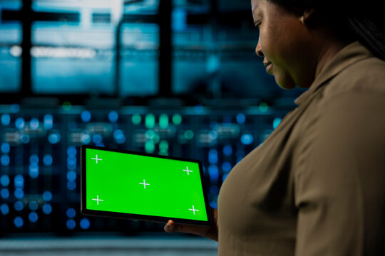 Close up of admin holding green screen tablet walking through server room rows with storage rigs. IT expert using chroma key device to inspect data center helping power internet services - Powered by Adobe