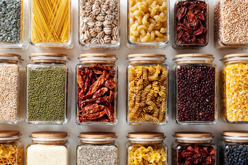 Neatly organized pantry: top-view of glass jars filled with pasta, grains, beans, seeds and dried chilies for stylish kitchen storage