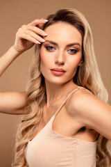 Fototapeta premium Elegant blonde woman with glamorous makeup posing against a beige vertical background showcasing beauty