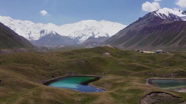 Panoramic flying drone movement over blue lakes at 3600m Base Camp, offering a vast panoramic view of the Pamir Mountains and lenin Peak wall.  Ibn Sina expedition in Kyrgyzstan, Central Asia.