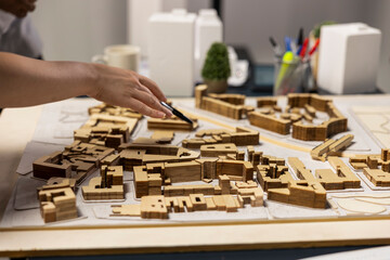 Close up of developers arranging 3D models to explore residential layout options, working on structural city planning for urban development project during a strategic team meeting.