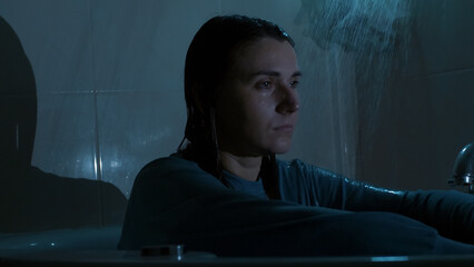 A young woman sits under running shower water at night, overwhelmed and emotionally drained. Dark, cold tones and dramatic lighting reflect sadness, stress, and mental struggle. 