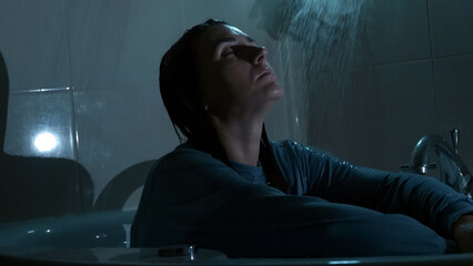 A young woman sits under running shower water at night, overwhelmed and emotionally drained. Dark, cold tones and dramatic lighting reflect sadness, stress, and mental struggle. 