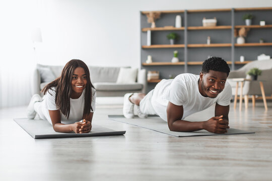 Healthy Lifestyle Concept. Joyful millennial black man and woman planking together at home and smiling, happy couple doing abs exercises tabata on floor in living room at modern apartment